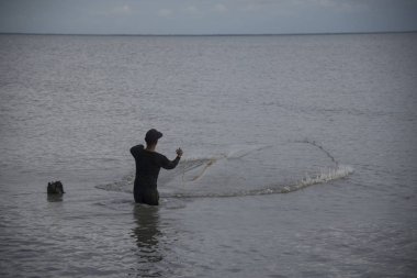 Perak, Malezya.7 Mayıs 2019: Tanjung Sepah plajında karides yakalamaya çalışan yüksek gelgit sırasında deniz kenarında duran Malay adam denize ağ dökme, Lekir.
