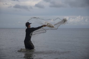 Perak, Malezya.7 Mayıs 2019: Tanjung Sepah plajında karides yakalamaya çalışan yüksek gelgit sırasında deniz kenarında duran Malay adam denize ağ dökme, Lekir.