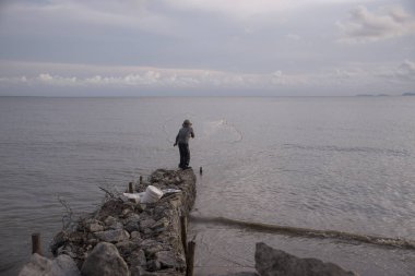 Perak, Malezya.7 Mayıs 2019: Tanjung Sepah plajında karides yakalamaya çalışan yüksek gelgit sırasında deniz kenarında duran Malay adam denize ağ dökme, Lekir.
