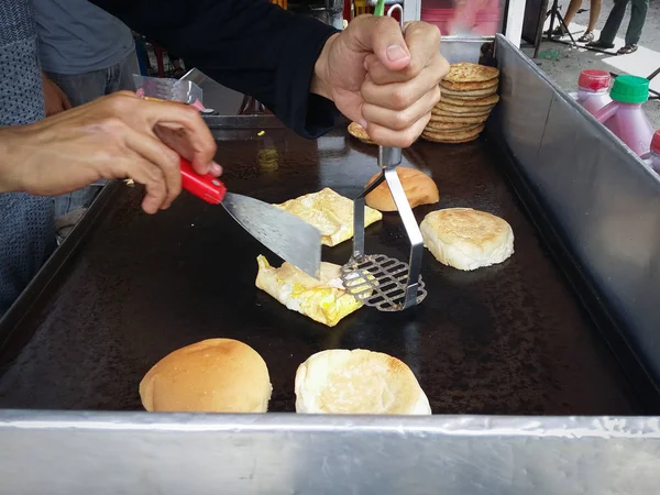 someone unrecognized preparing meat and egg burger