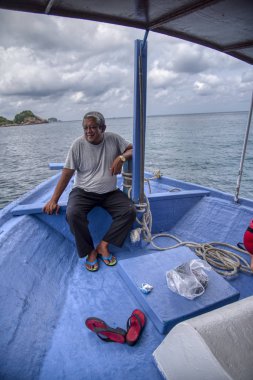Trengganu, Malezya. 24 Haziran 2019 : Yaşlı malay adam Redang Adası'nda tekne yolculuğu zevk rıhtım ahşap bankta oturdu. 
