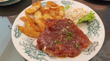 Baharatlı soslu bir tabak kızarmış tavuk pirzolası dilimlenmiş patates ve lahana mayonezi..