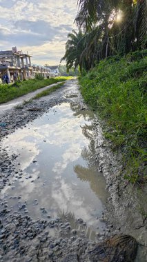 Kırsal toprak yolda sağanak yağış sonrasında durgun su havuzu yansıtıyor. 