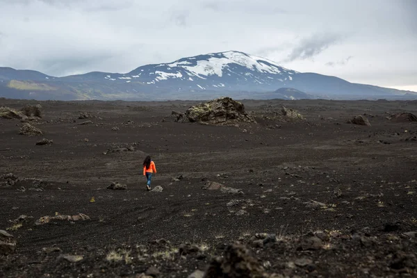 Una ragazza con una giacca arancione cammina attraverso un campo di lava bruciato — Foto Stock