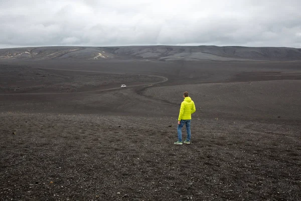 Un uomo è in piedi su un campo di lava e guardando in lontananza su una macchina in partenza — Foto Stock