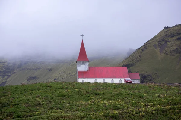 Un'unica chiesa cattolica bianca con tetto rosso sorge su una collina verde tra le montagne, sullo sfondo una fitta nebbia — Foto Stock