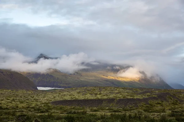 Lava veld bedekt met mos en korstmossen, op de achtergrond u bergen in witte wolken te zien — Stockfoto