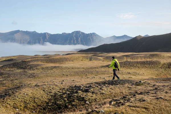 Un turista con chaqueta amarilla camina al amanecer hacia las montañas y la niebla — Foto de Stock