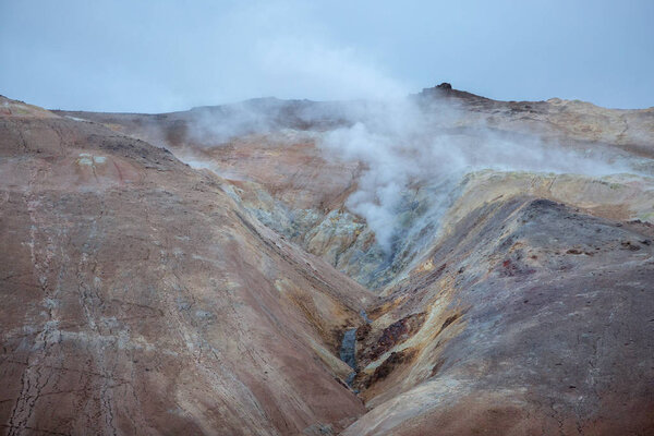 Sulfur smoke erupts from the ground between red volcanic rocks.