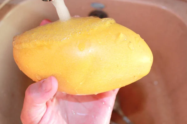 Gelbe Mango in der Hand unter dem Wasser in einer braunen Spüle — Stockfoto