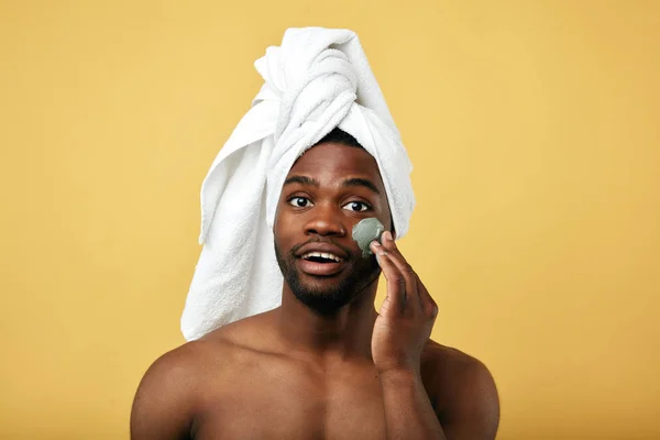 Young happy man with a towel on his head applying mask on his face — 스톡 사진