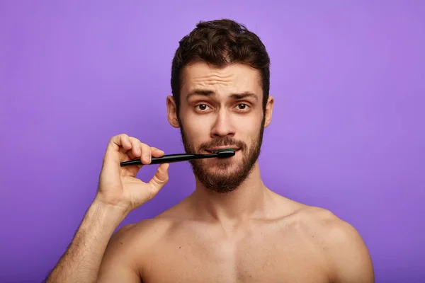 Schöner junger Mann beim Zähneputzen vor blauem Hintergrund — Stockfoto