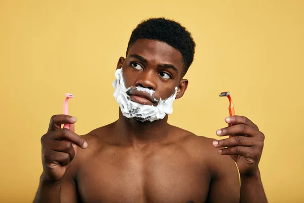 morning routine. Irritated puzzled man going to shave beard, isolated over yellow background.