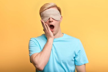 Genç adam uyku maskesi takmış ağzında plakla esniyor.