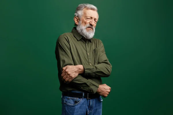Yeşil t-shirt ve dar pantolon içinde yaşlı adam ağrı dirseğini tutan kapalı gözleri ile — Stok fotoğraf