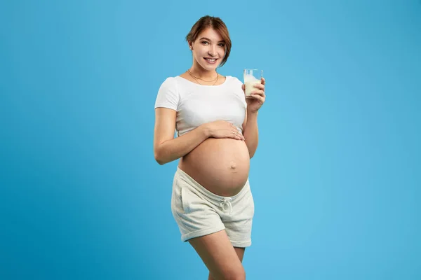 Positive schwangere Mädchen hält ein Glas Milch und berührt ihren Bauch — Stockfoto