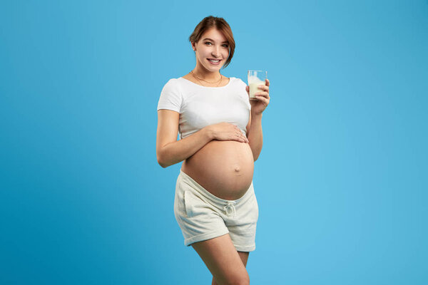 positive pregnant girl holding a glass of milk , touching her belly