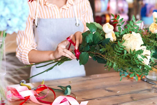 Owner of florist shop tying red ribbon around bunch of fresh white roses