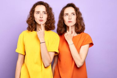 şık genç iki özdeş kadın çenesine dokunarak ve yukarı bakıyor