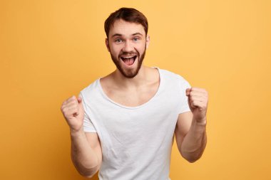 sarı arka plan üzerinde izole başarı kutlayan memnun olumlu genç adam