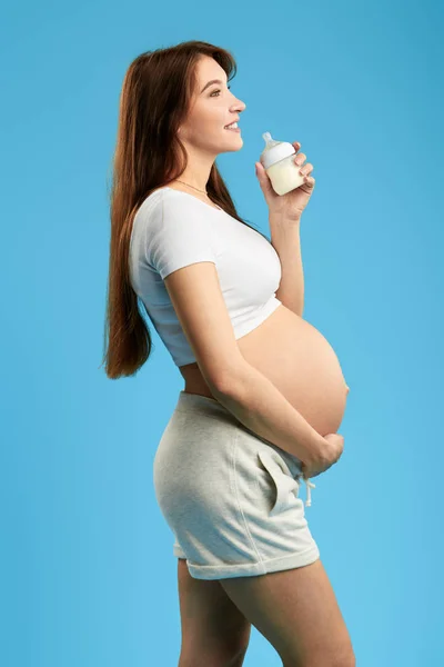 Lustige schwangere Mädchen berühren ihren großen Bauch und gehen, Milch zu trinken — Stockfoto