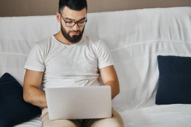 kanepede dizüstü bilgisayar ile oturan gözlük yakışıklı akıllı adam