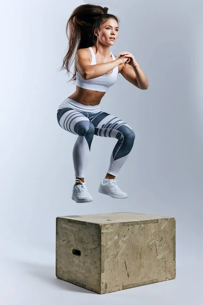 well-built sweaty girl doing box jump at sport center
