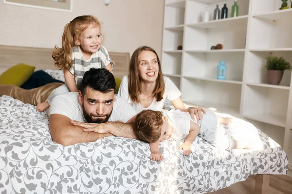 Tired unhappy depressed man lying on the bed with his happy wife and children — Stock Photo, Image