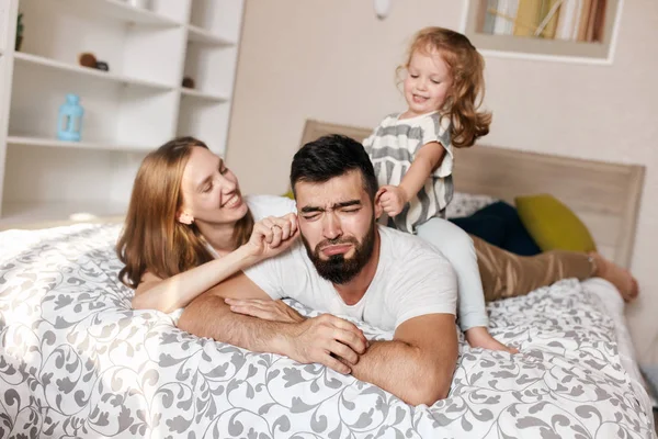 Cheerful smiling wife and her daughet pulling their unhappy crying daddys ears — Stock Photo, Image