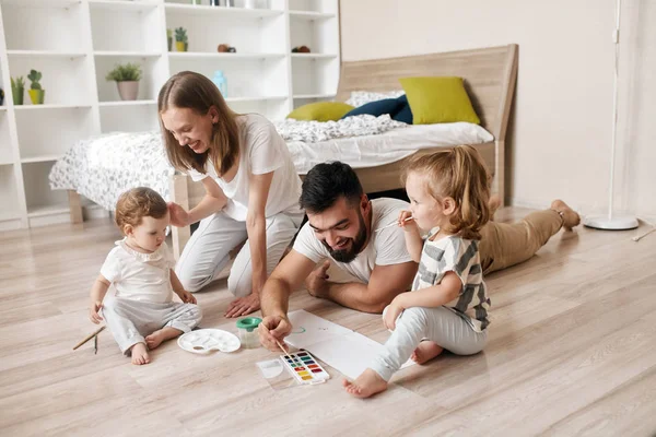 Positiv pappa, mamma, barn maler med pensler mens de sitter på gulvet – stockfoto