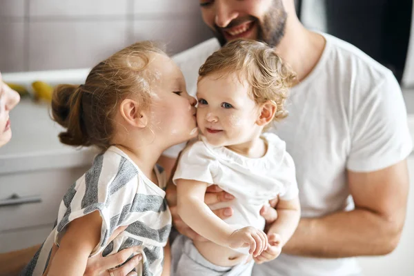 Elder sister kissing her little sister while sitting on their father — Stock Photo, Image