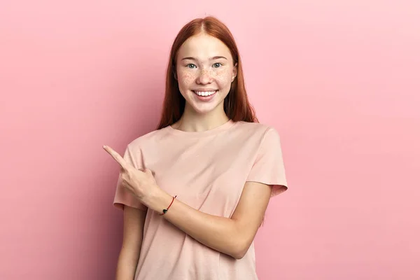 Red-headed happy woman pointing finger to the side