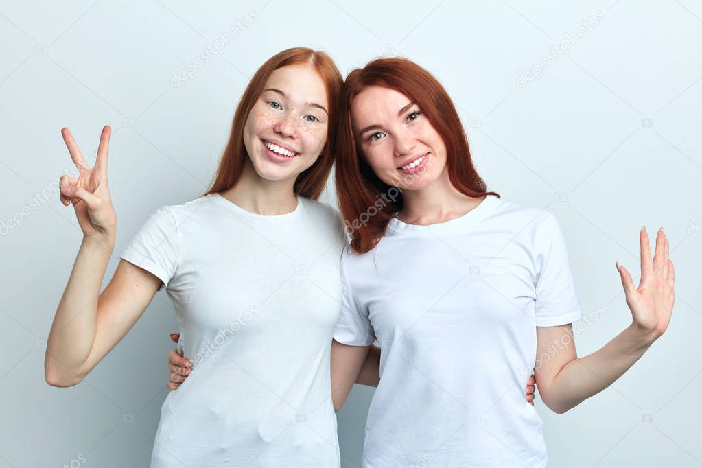 two positive girl embracing each other and showing victory gesture