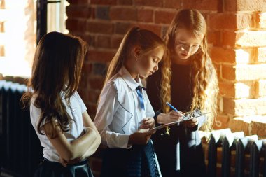 üç küçük kız notlar yapıyor, kağıda bir şeyler yazıyor.