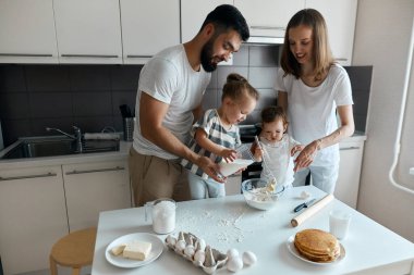 İki küçük kız anne ve babalarına macun yapmalarında yardım ediyor.