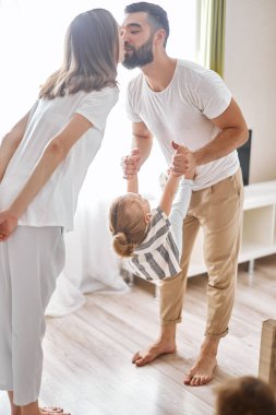 İki ebeveyn birbirlerini öperken çocukları babalarına tırmanıyor.