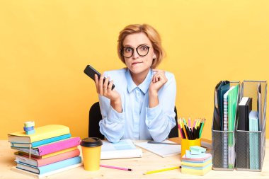 Şaşırmış, ciddi bir kadın elinde akıllı bir telefonla masada oturuyor.