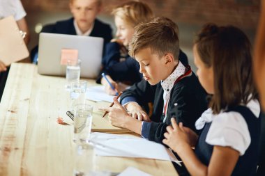 Küçük çocuklar, liderleri konferans verirken notlar alıyorlar.