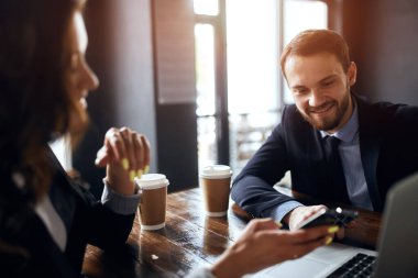 Akıllı telefonunu sakallı meslektaşına gösteren çekici bir kız.