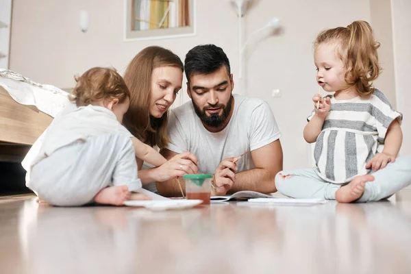 Fiatal szülők időt töltenek gyermekeikkel, segítenek nekik a házi feladat elkészítésében — Stock Fotó