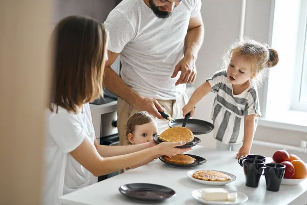 Hardworking young girl helping her parents to cook pancakes — Stock Photo, Image