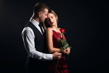 Kırmızı elbiseli romantik kadın gül tutuyor ve erkeğe bakıyor..