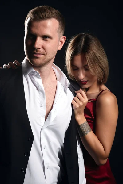 romantic blonde woman in elegant red dress standing behind her boyfriend