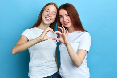 Gülümseyen iki güzel kız elleriyle kalp figürü yapar.