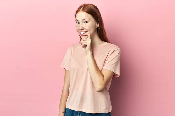 Cheerful woman touching her lips while thinking, isolated pink studio background — Stock Photo, Image