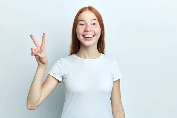 Atrakcyjna pozytywna dziewczyna z piegami pokazuje znak pokoju i uśmiech. — Zdjęcie stockowe