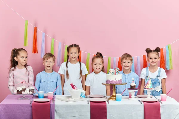 Crianças adoráveis tímidas em pé atrás da mesa olhando para a câmera — Fotografia de Stock