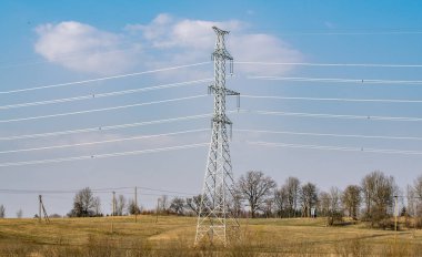 Bulutlarla mavi gökyüzüne karşı yüksek voltajlı güç hatlarını destekler.