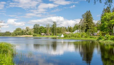 Yeşil ormanlarla çevrili bir göl ile doğal yaz manzara. Mavi gökyüzündeki beyaz bulutlar.