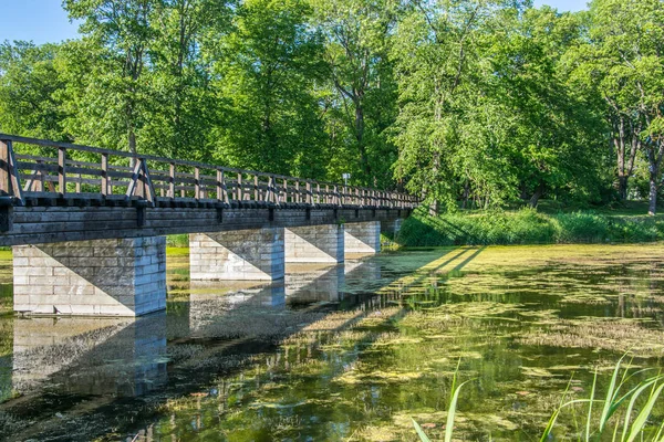 Most nad rzeką w parku miejskim. Drewniany most na pali ceglanych. — Zdjęcie stockowe